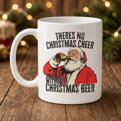A white mug on a wooden table shows Santa drinking beer and the slogan “There’s no Christmas cheer without Christmas beer,” with warm festive lights behind it.