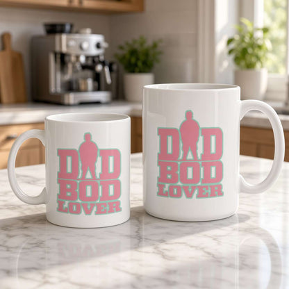 Two white ceramic mugs on a marble kitchen counter, both printed with pink-and-teal “Dad Bod Lover” lettering; a larger mug sits beside a smaller one.