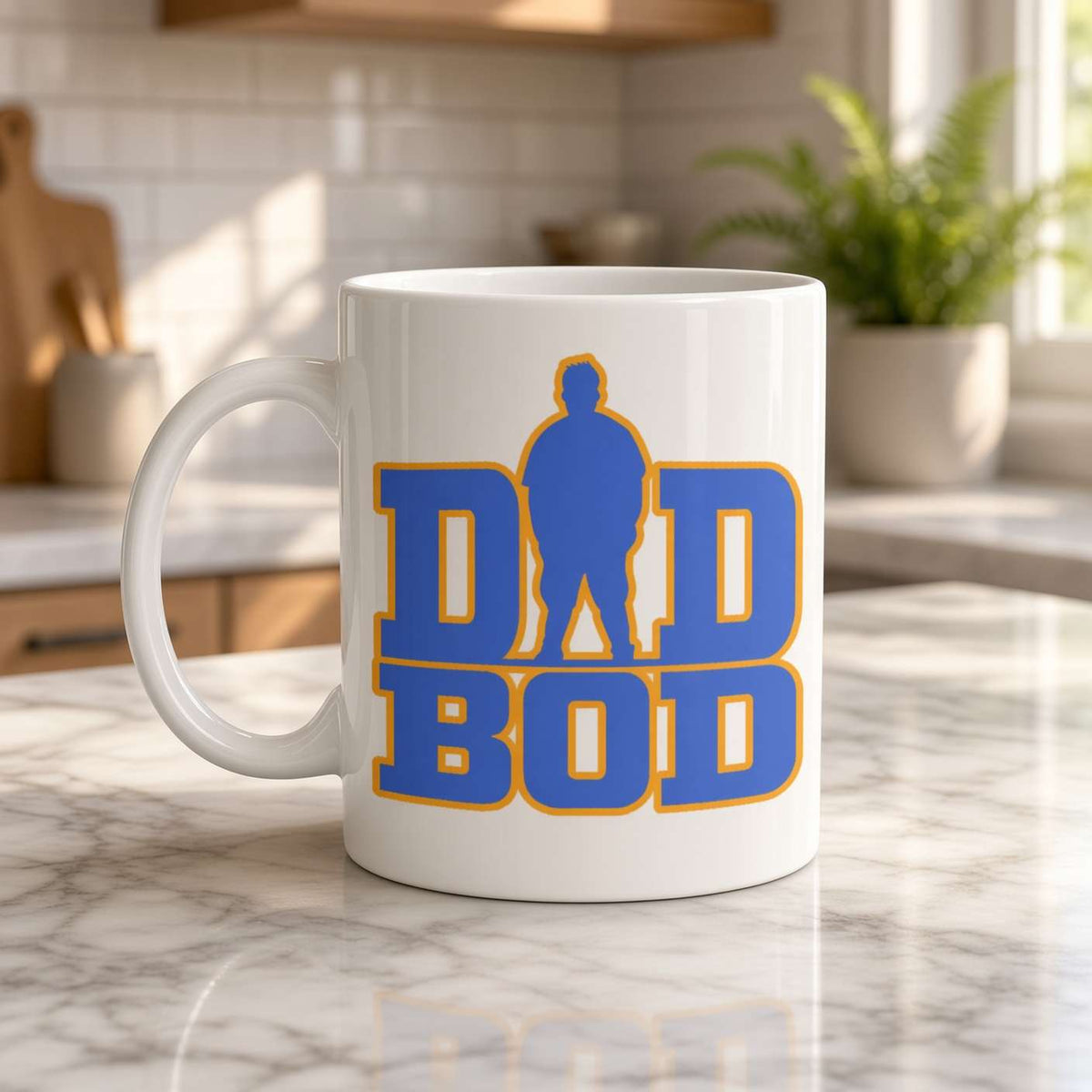 A white ceramic coffee mug with a blue and yellow 'DAD BOD' graphic, sitting on a marble kitchen counter with a blurred kitchen background.