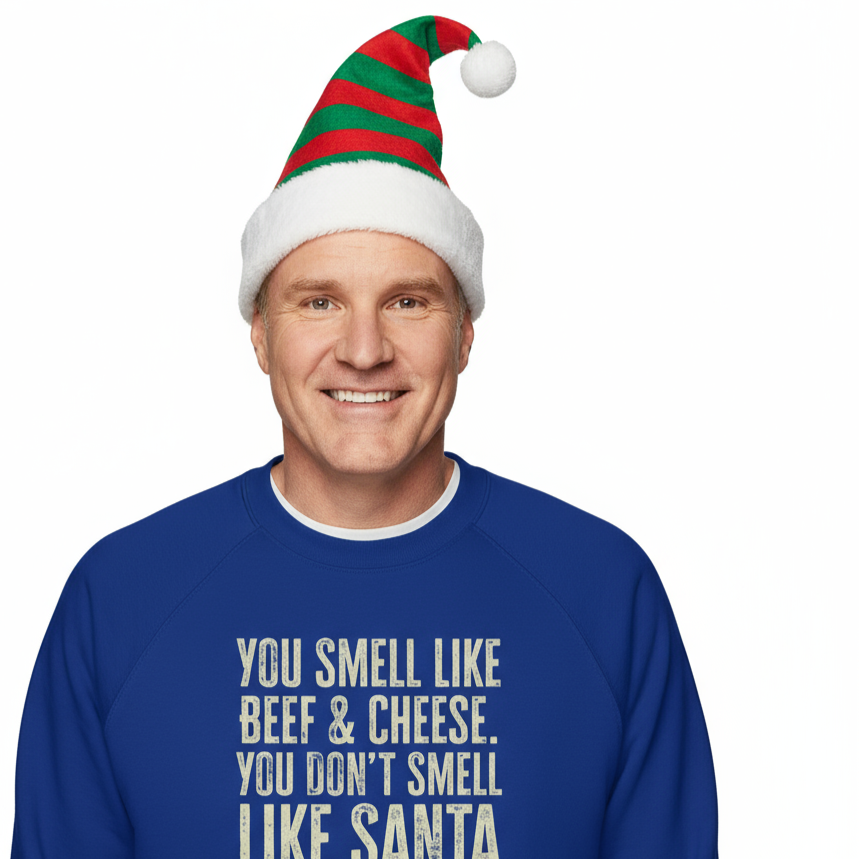 Man wearing a blue Christmas sweater with humorous Elf text "You Smell like Beef & Cheese" and a festive hat on a white background