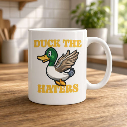 White mug on a sunlit wooden kitchen counter, featuring a cheerful cartoon duck and bold yellow “DUCK THE HATERS” text; playful, upbeat tone.