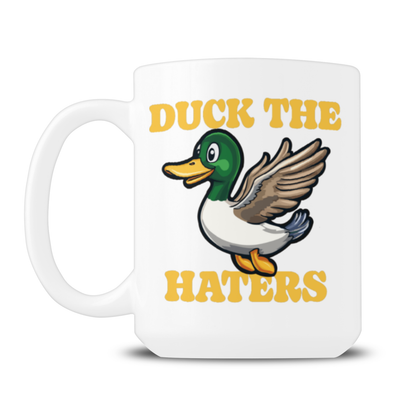 White ceramic mug featuring a cartoon mallard, wings raised between bold yellow “DUCK THE HATERS” text; playful, upbeat design on a plain background.