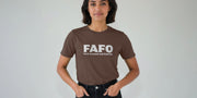 A Woman stands against a plain background wearing a brown Offensive Slogan T-shirt with 