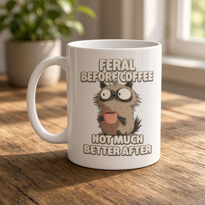 White mug featuring a wide-eyed, shaggy animal holding a tiny cup, with the joke “Feral before coffee, not much better after”—playful, sleepy humor.