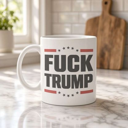 A white ceramic mug on a marble kitchen counter reads “FUCK TRUMP” in bold lettering with red stripes and stars; the bright kitchen feels calm and homey.