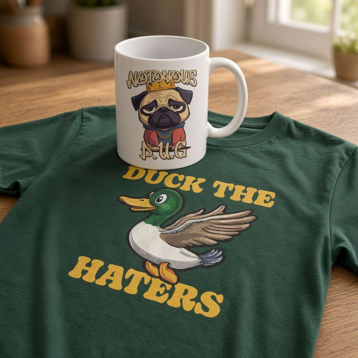 A white “Notorious P.U.G.” mug sits on a green T-shirt with a cartoon duck and yellow “DUCK THE HATERS” text in a cozy, sunlit room.