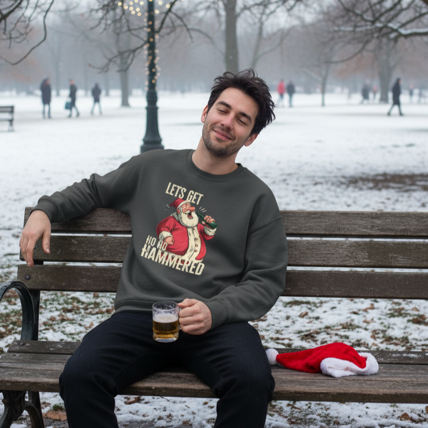 Man sitting on a bench in a snowy park wearing a funny Christmas sweatshirt with a humorous Santa Claus graphic.
