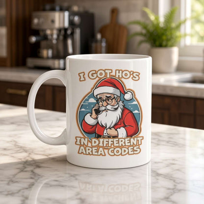 White mug on a marble kitchen counter shows a winking Santa and the slogan “I got Ho’s in different area codes,” giving the cozy scene playful humor.