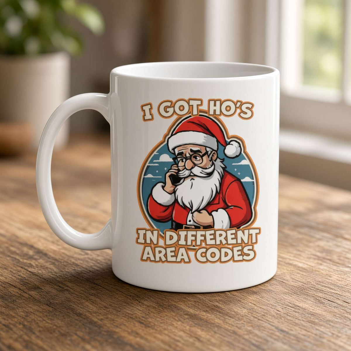 A white mug on a wooden table shows a cartoon Santa on the phone with the joke “I got Ho’s in different area codes,” in a cozy, playful setting.