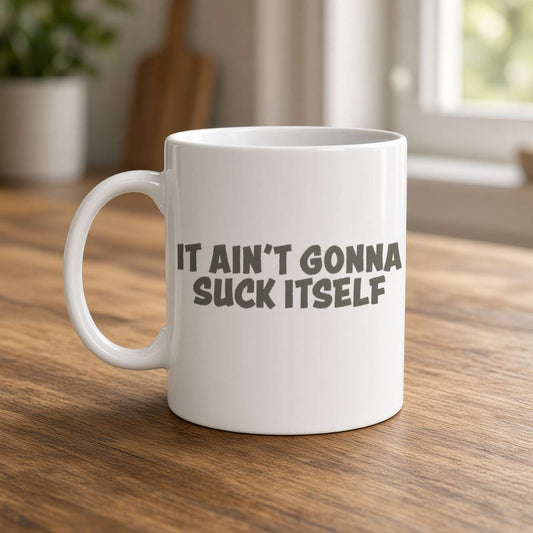 A white ceramic mug on a wooden table reads “It ain’t gonna suck itself,” with a softly lit kitchen background and a cheeky, humorous tone.