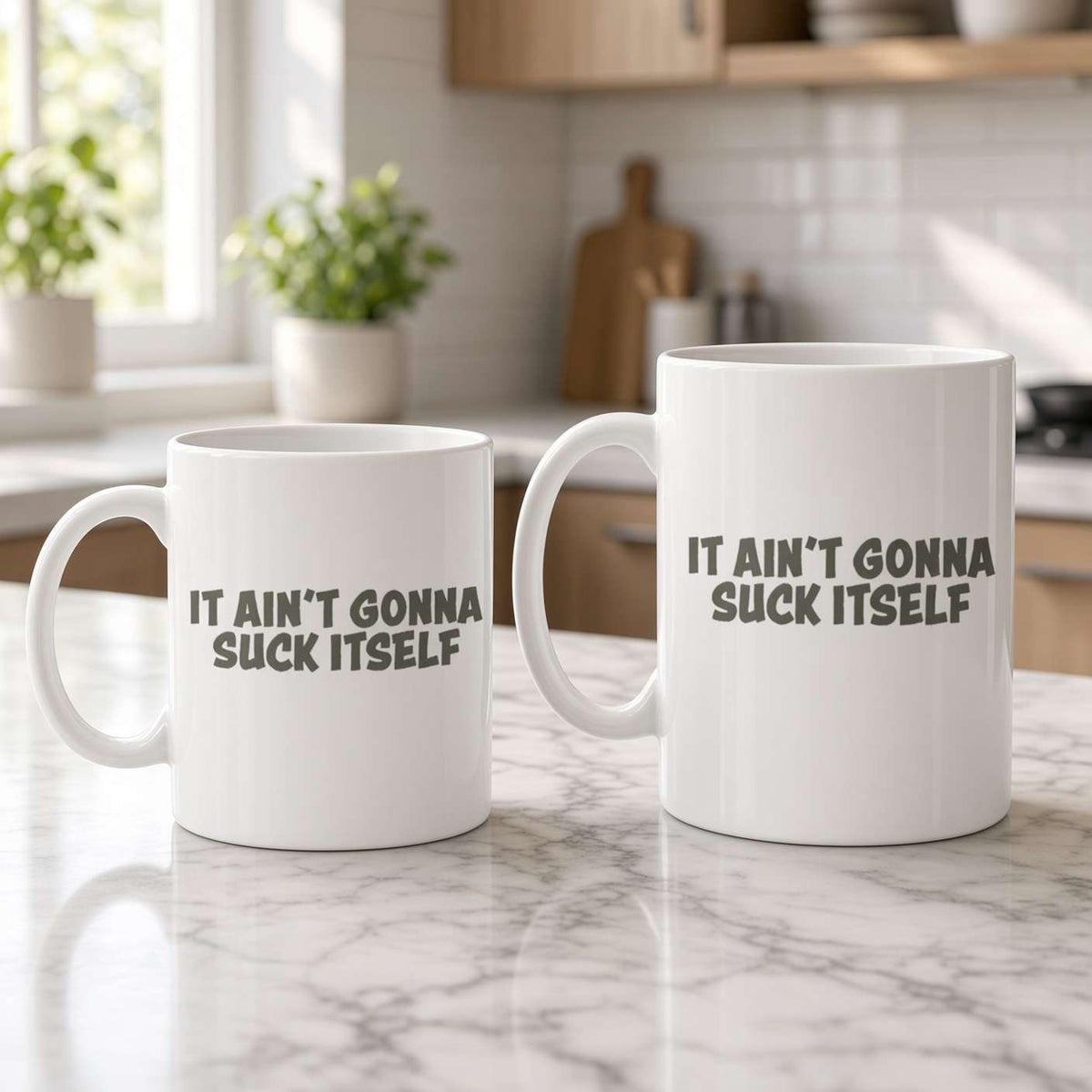 Two white coffee mugs on a marble kitchen counter read “It ain’t gonna suck itself”; soft daylight and greenery create a bright, playful mood.