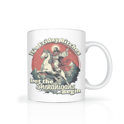 A white ceramic mug with a humorous graphic of Jesus riding a white unicorn against a red sun background, with the text 'It's Friday Bitches' and 'Let the Shenanigans Begin'.