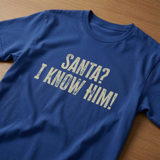 Blue Santa? I Know Him! t-shirt laid flat on a wooden surface showing the full distressed slogan, fun mens witty Christmas film slogan design full of pure attitude