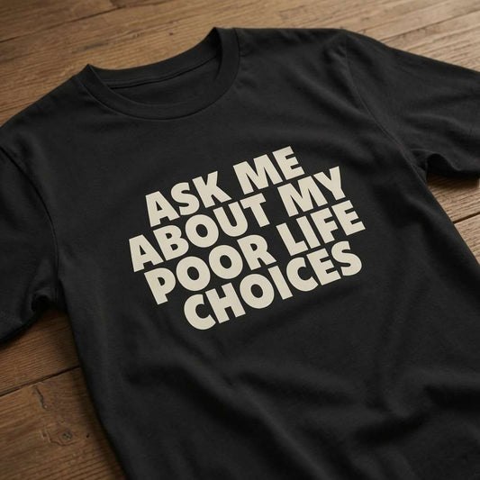 Black Ask Me About My Poor Life Choices t-shirt laid flat on a wooden surface showing the full white slogan, funny relatable ladies statement shirt that every no-nonsense lady will claim