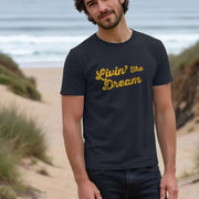 A man stands on a beach path, wearing a navy funny quote t-shirt with 