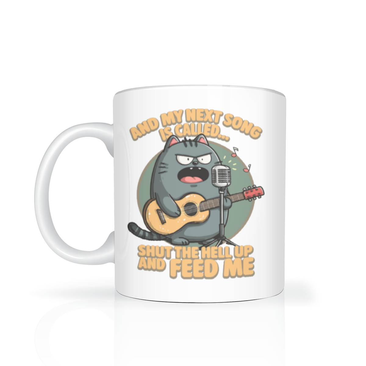 A white mug features a grumpy gray cat playing guitar at a microphone, with the caption “And my next song is called: Shut the hell up and feed me,” in humorous lettering.