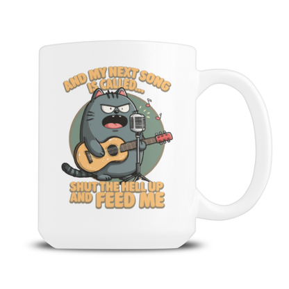 White mug featuring a grumpy gray cat playing guitar at a microphone, with the joke “Shut the hell up and feed me”; humorous, irreverent tone.