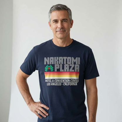 Man with grey hair smiling hand on hip in navy Nakatomi Plaza t-shirt, fun the ultimate mens christmas