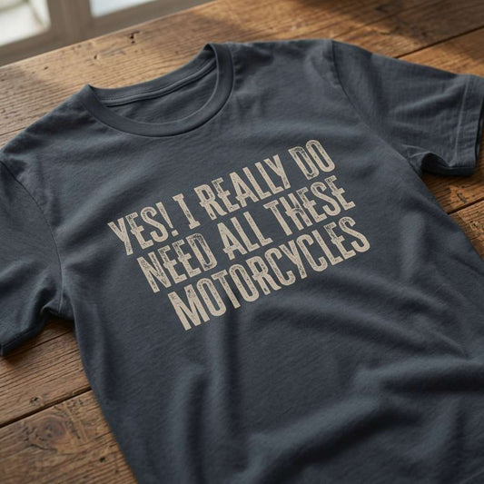 Ink grey t-shirt laid flat on a wooden table featuring the distressed text “Yes! I Really Do Need All These Motorcycles”, perfect for the dedicated biker who refuses to apologise for his collection