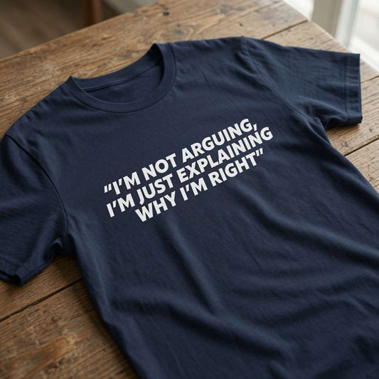 Navy blue t-shirt laid flat on a wooden table with the white slogan “I’m Not Arguing, I’m Just Explaining Why I’m Right”, classic witty and relatable mens quote design