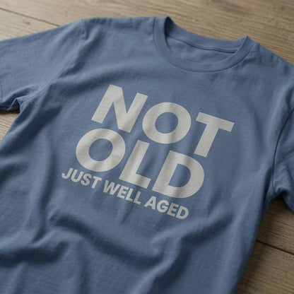 Blue Not Old Just Well Aged t-shirt laid flat on a wooden surface showing the full slogan, funny mens cheeky grandad gift slogan design full of pure attitude