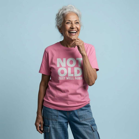 Older woman with white hair laughing with one hand near her chin while wearing a pink Not Old Just Well Aged t-shirt, funny and witty age banter for ladies