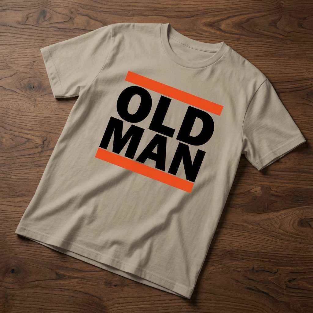 Beige Old Man t-shirt laid flat on a wooden surface showing the bold black text framed by orange bars, simple and funny dad design