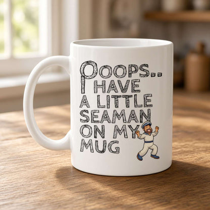 A white ceramic mug with a humorous seaman-themed graphic printed on it, sitting on a wooden table in a softly blurred indoor setting near a window.