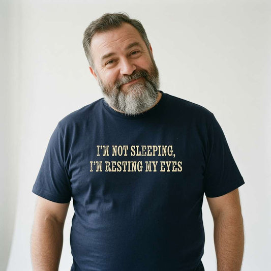 Bearded man smiling slightly while wearing a navy I’m Not Sleeping, I’m Resting My Eyes t-shirt, humorous slogan dad gift design
