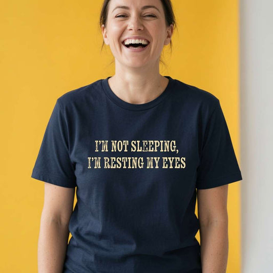 Woman laughing while wearing a navy I’m Not Sleeping, I’m Resting My Eyes t-shirt, humorous ladies relatable funny quote design full of pure attitude