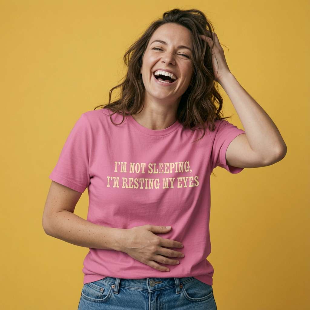 Woman laughing with one hand in her hair and one on her stomach while wearing a pink I’m Not Sleeping, I’m Resting My Eyes t-shirt, witty ladies funny relatable slogan design full of pure attitude