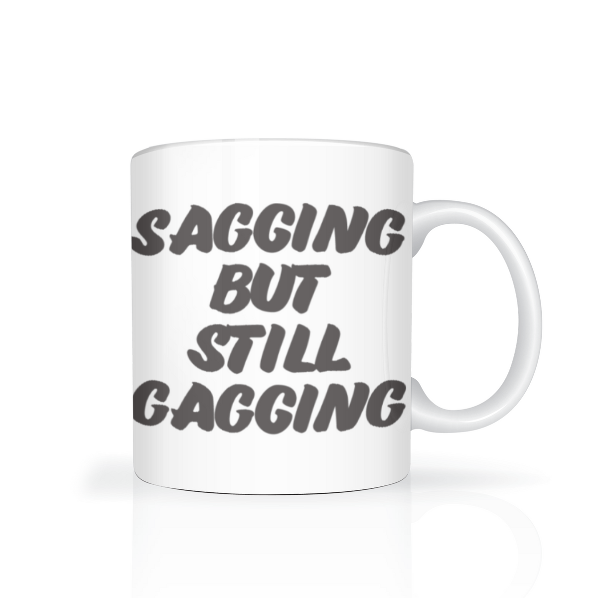 White mug with bold dark lettering reading “Sagging but still gagging,” a cheeky, irreverent slogan on a clean white background.