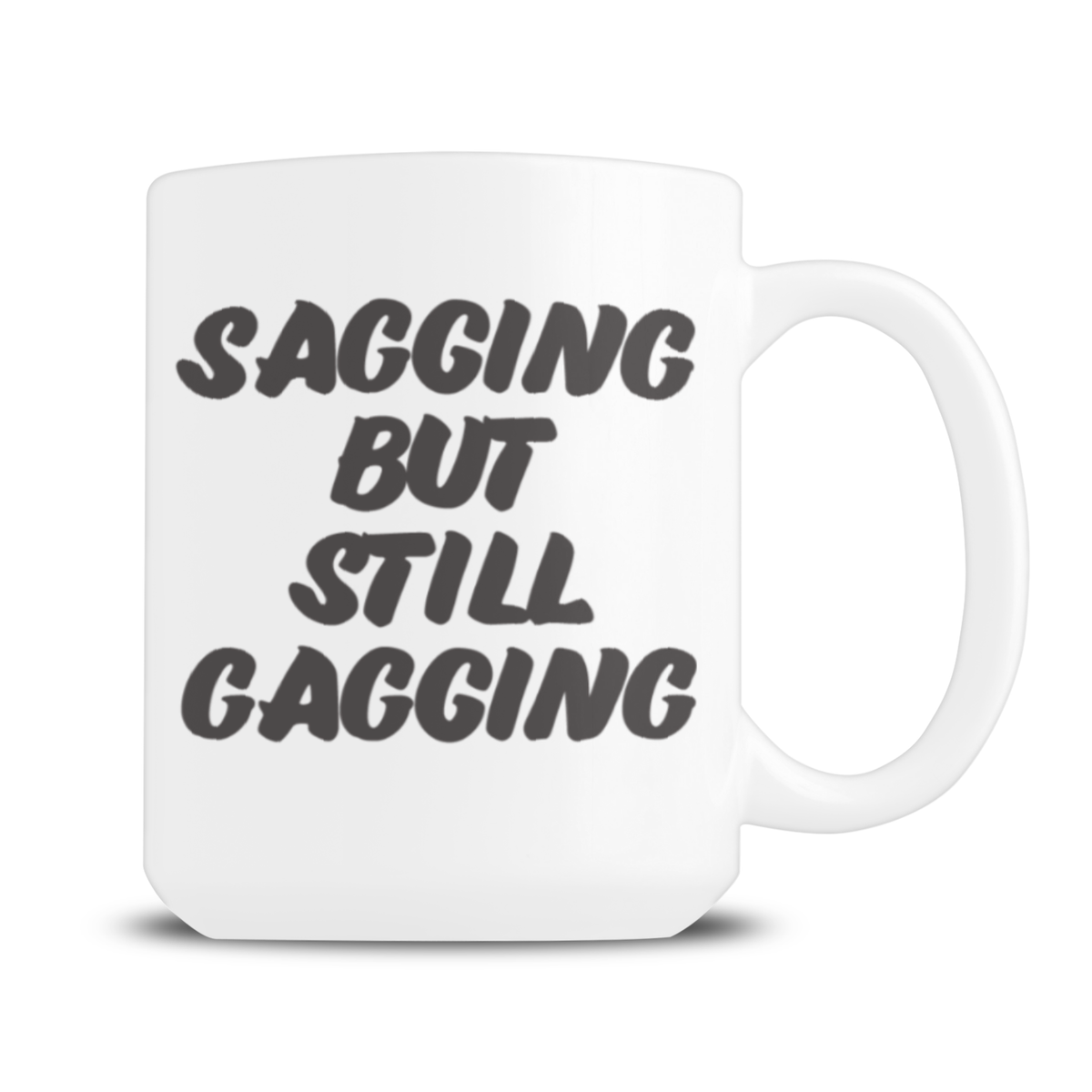 White ceramic mug with bold black lettering reading “SAGGING BUT STILL GAGGING,” a cheeky, humorous slogan, displayed against a plain white background.
