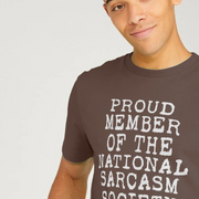 Smiling man wearing a brown funny T-shirt with white text reading, 
