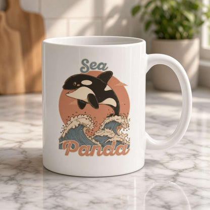 A white ceramic mug on a marble counter features a playful orca leaping over stylized ocean waves beneath the word “Sea,” in a warm, sunny kitchen.