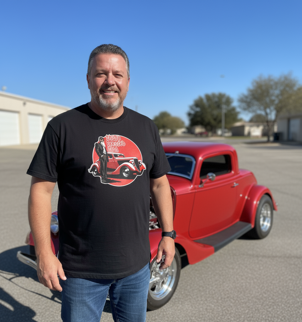Man wearing a black music inspired t-shirt with a graphic design standing in front of a red classic car.