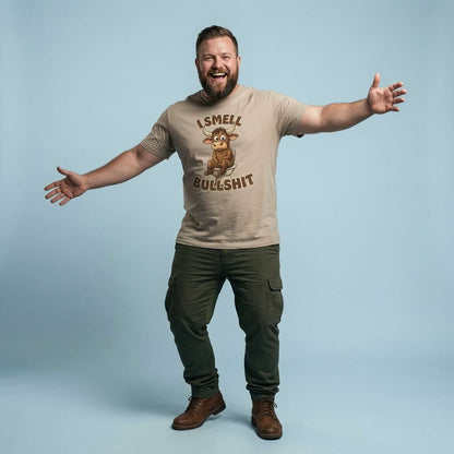 Bearded man laughing with arms outstretched while wearing a stone I Smell Bullshit t-shirt featuring a cartoon bull on the toilet, funny and rude mens bull pun