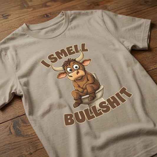Beige I Smell Bullshit t-shirt laid flat on a wooden surface showing the full toilet-sitting bull graphic, funny and witty rude bull pun design