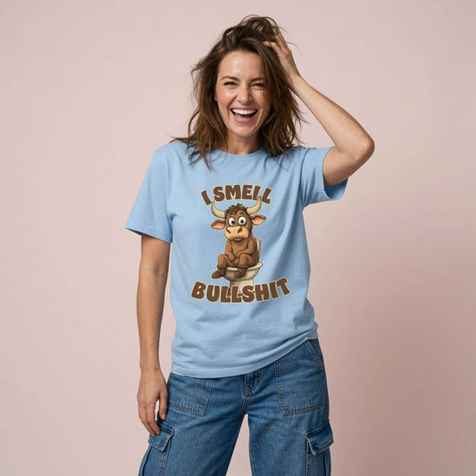Woman laughing with one hand in her hair while wearing a sky blue I Smell Bullshit t-shirt featuring a cartoon bull on the toilet, funny and witty rude bull pun