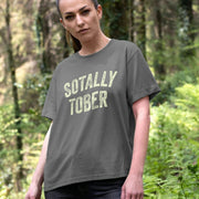 A woman stands in a forest wearing a gray Festival t-shirt with the phrase 