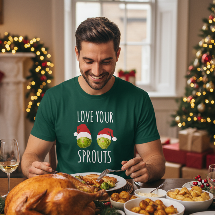 Man wearing a green funny Christmas t-shirt with 'Love Your Sprouts' text and Christmas-themed design, sitting at a festive dinner table.