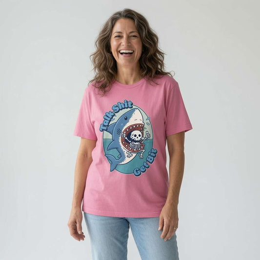 Woman laughing while wearing a pink Talk Shit Get Bit t-shirt featuring a shark swallowing a skeleton, witty and rude kawaii shark tattoo design for ladies