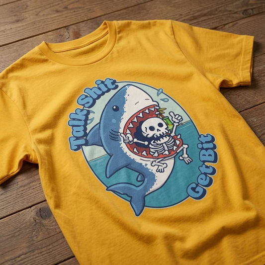 Yellow Talk Shit Get Bit t-shirt laid flat on a wooden surface showing the full shark and skeleton graphic, fun and rude kawaii shark relatable ladies slogan