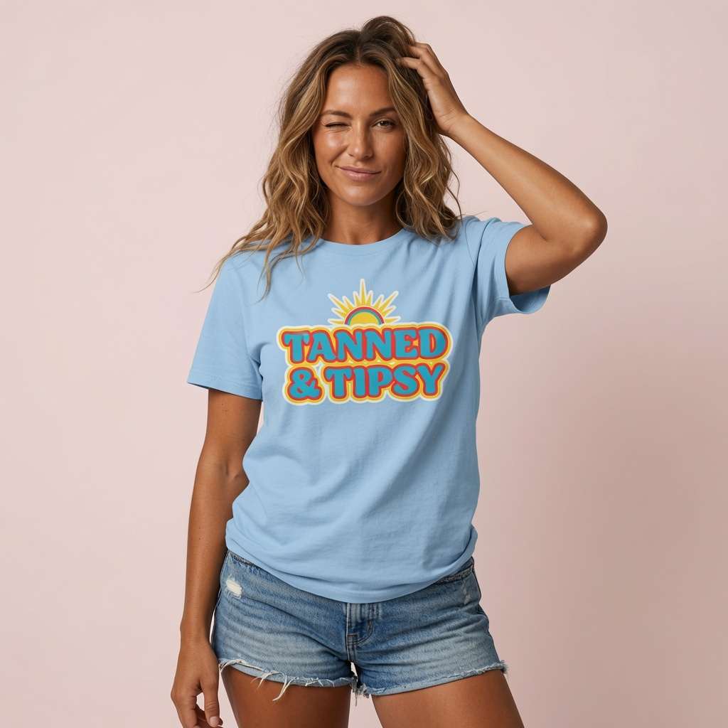 Woman winking with one hand in her hair while wearing a sky blue Tanned & Tipsy t-shirt featuring a colourful sun graphic, cheeky and fun ladies summer hen slogan