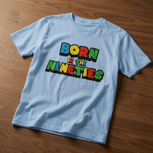 Sky blue Born in the Nineties t-shirt laid flat on a wooden surface showing the full colourful lettering, mens fun 90s video gamer inspired age-related shirt that every 90s kid will claim