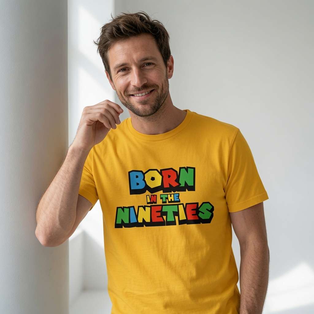 Man smiling with one hand near his chin while wearing a yellow Born in the Nineties t-shirt with bold multicoloured 90s-style lettering, mens 90s video gamer inspired fun age-related shirt
