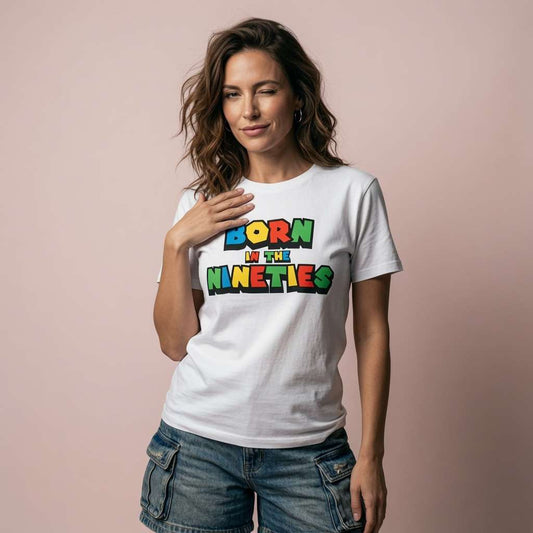 Woman with one hand on her chest while wearing a white Born in the Nineties t-shirt with bold multicoloured 90s-style lettering, ladies 90s gamer inspired fun age-related shirt