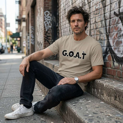 Man sitting against a brick wall in a beige G.O.A.T t-shirt, legendary mens animal pun slogan dad gift that every cheeky lad will claim