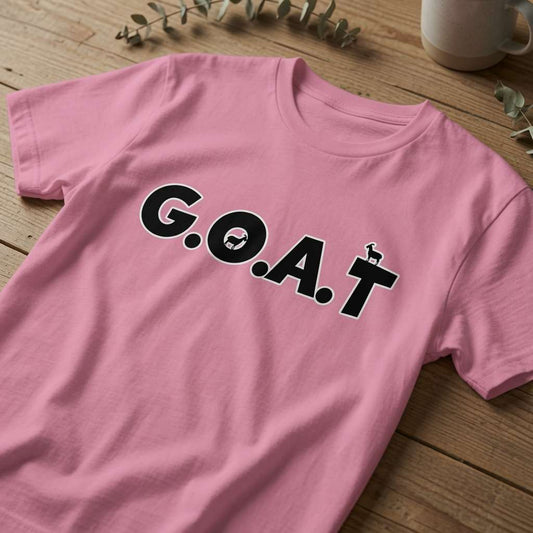 Pink G.O.A.T t-shirt laid flat on a wooden surface showing the full lettering and goat icons, witty legendary ladies slogan shirt that every no-nonsense lady will claim