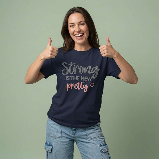 Woman smiling and giving double thumbs-up while wearing a navy Strong is the New Pretty t-shirt, ladies fun motivational strong quote design